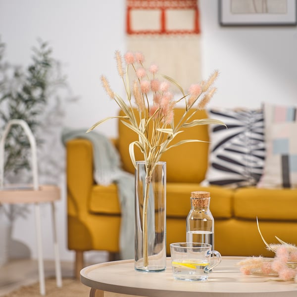 Yellow couch, wooden coffee table, white side table. Vase with pink-beige flowers, small glass bottle, mug with yellow handle.