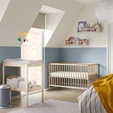 Baby nursery with light blue walls, light wood crib, changing table, shelves, and yellow accents.
