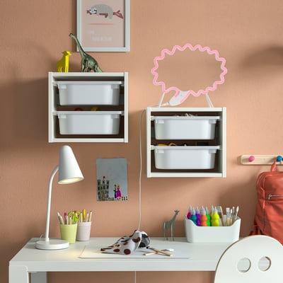 Kids desk with SNÖDJUP storage, toys, lamp, backpack, art supplies, giraffe, peach wall, art.