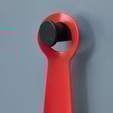 Red metal shoehorn hangs neatly on wall hook. Bright, compact design for easy use and storage.