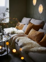 Cozy living room with grey SÖDERHAMN sofa, brown pillows, sheepskin, and christmas decorations - including hanging lights and pine branches.
