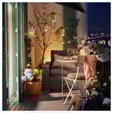 Cozy balcony setup with SOLLERÖN dark gray outdoor furniture, white cushions, potted flowers, and hanging lanterns.