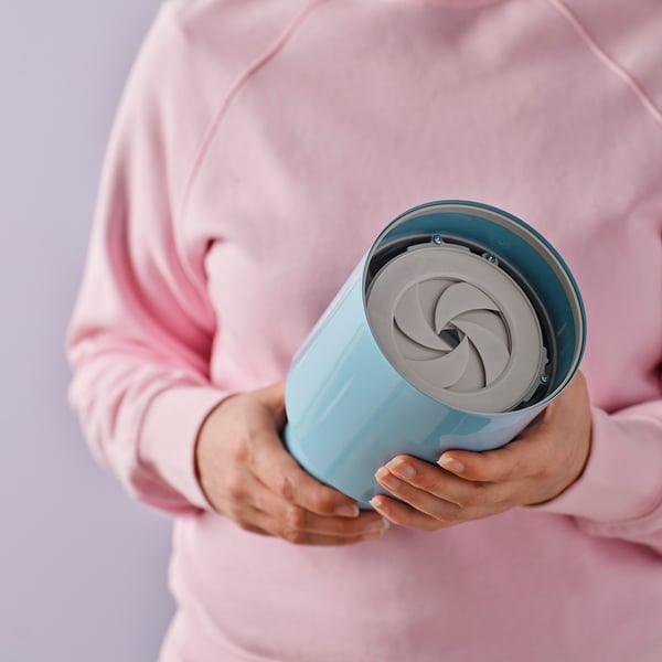 A person holds a blue SPETSBOJ table lamp, which emits soft light upwards and downwards, adjustable by turning the shade.