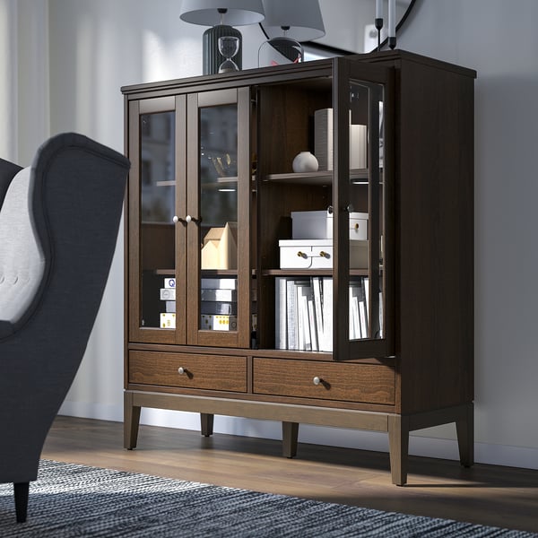 Large dark wood cabinet with glass doors and drawers, holding books, boxes, and decor next to a grey chair.