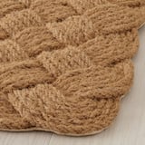 Handmade natural coir doormat with thick weave on light wood floor. Shows texture and craftsmanship.