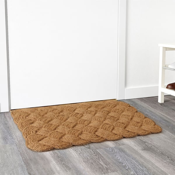 Woven coir doormat near white door, trapping dirt on grey floor.
