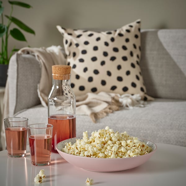 Bowl of popcorn and drinks on table. Sofa with pillows and blanket.