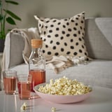 Bowl of popcorn and drinks on table. Sofa with pillows and blanket.