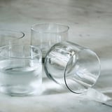 Three mouth-blown glass cups on light surface. One tipped with ice cube nearby.