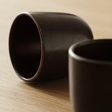 Dark stoneware mugs, subtle speckles, rustic design, placed on wooden surface.