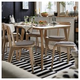 Modern dining scene with light wood table, four matching chairs with grey and patterned cushions, black and white striped rug.