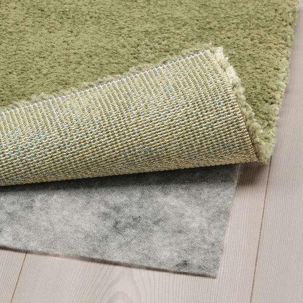 Light green, plush rug folded on wooden floor, revealing thick, textured backing, suggesting comfort and durability.