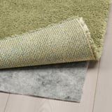 Light green, plush rug folded on wooden floor, revealing thick, textured backing, suggesting comfort and durability.