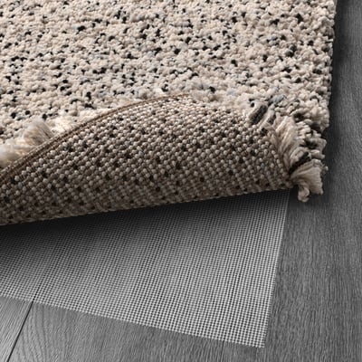 A folded textured rug on a mesh anti-slip underlay. The underlay prevents slipping and keeps the rug in place on various types of flooring.