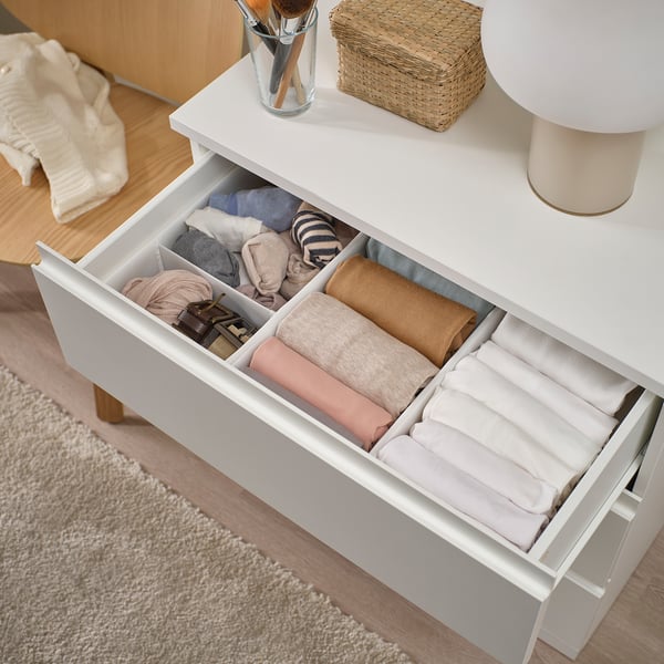 Organised dresser drawer with folded clothes. Top holds makeup brushes, basket, and lamp.