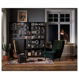 Home music room with large speaker shelves, green chair, guitar, vintage amp, vintage rug, cactus, lamp on wooden floor.