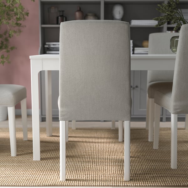 Modern dining set with light grey chairs, white table, pink walls, and bookshelf.