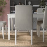 Modern dining set with light grey chairs, white table, pink walls, and bookshelf.