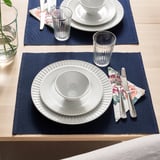 Two place settings with plates, bowls, cups, cutlery, and napkins on dark blue mats.