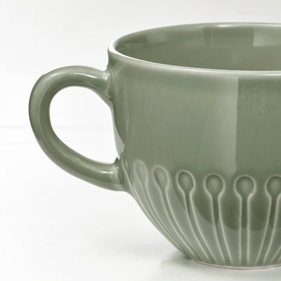 This image shows a green STRIMMIG mug. Made of stoneware, it has a smooth body with embossed flower patterns. It is round with a handle on the right.