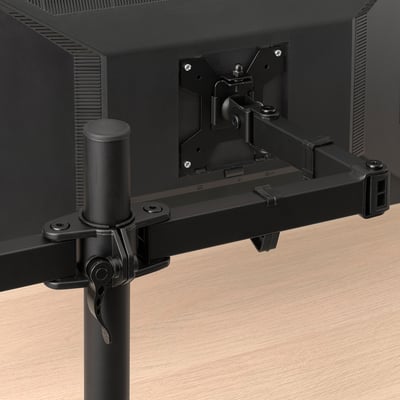 Black monitor arm securely clamps to wooden desk, offering adjustable screen positioning.