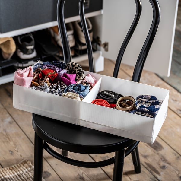 White storage box on black chair, holding colorful clothes and rolled belts.