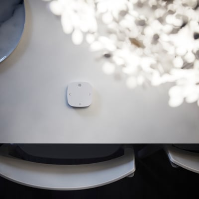 A white, square-shaped STYRBAR remote control made of abs plastic. It three illuminated symbols for controlling smart lighting.