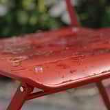 Red foldable metal table surface with water drops. Outdoor furniture.
