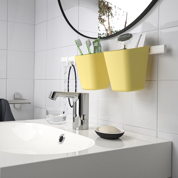 Modern bathroom with white sink, chrome faucet, round mirror, yellow SUNNERSTA organizer holding toothbrushes.