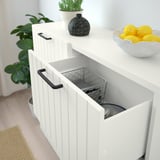 White storage cabinet with open door revealing mesh basket inside, lemons in bowl on top.