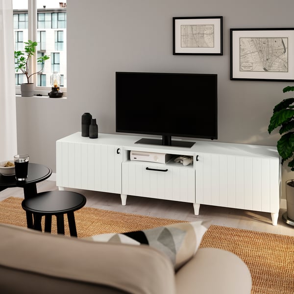 Modern living room with white SUTTERVIKEN tv stand, flat screen, and beige couch. Decorative maps and plants around.