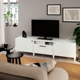 Modern living room with white SUTTERVIKEN tv stand, flat screen, and beige couch. Decorative maps and plants around.