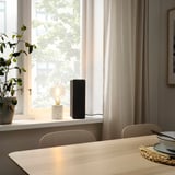 Modern dining area with SYMFONISK speaker & plants beside a large window.