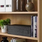 A sleek speaker placed on a wooden shelf, part of the SYMFONISK series, offering high-quality sound and smart streaming capabilities.