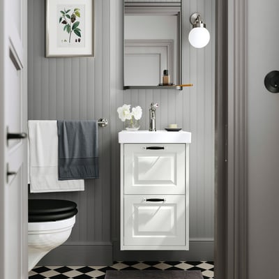 Modern white bathroom vanity, narrow fit, with beveled edges and two drawers, between gray walls and black toilet.