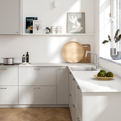 Modern white kitchen with light grey TÄRNHULT wall panel, larger than cooktop, featuring recycled glass.