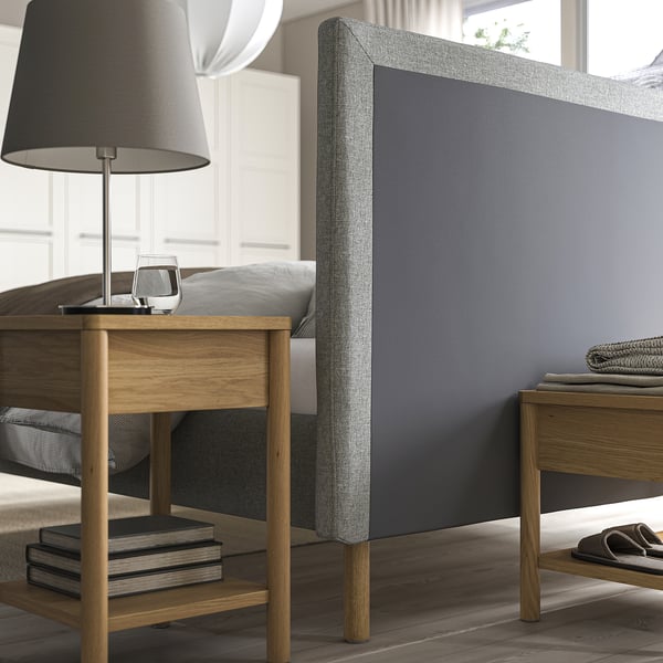 Cozy bed with soft, removable headboard cover and wooden side tables, one holding a lamp and the other some books.