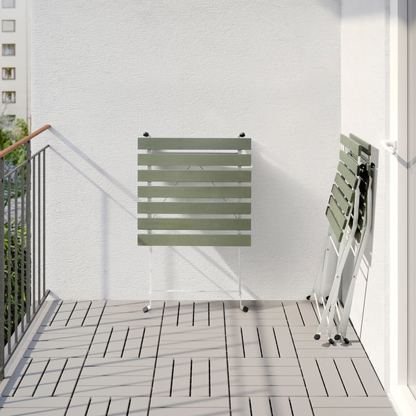 Balcony setup with foldable green TÄRNÖ table and chair against white wall. Easy to store and space-saving.
