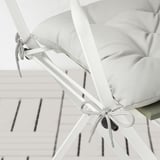 Modern white metal folding chair with light gray cushions secured by decorative ties, shown indoors against white wall.
