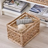 Woven basket containing knitting supplies, placed near a magazine rack.