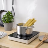 Portable induction hob with spaghetti, plant, whisk.
