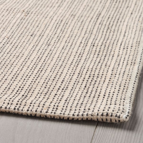 Close-up of TIPHEDE rug; soft, textured cotton weave, subtle patterns, laid on wooden floor.