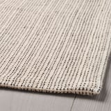 Close-up of TIPHEDE rug; soft, textured cotton weave, subtle patterns, laid on wooden floor.