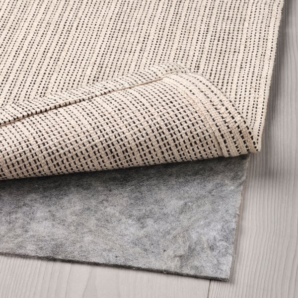 A folded beige cotton rug, perfect for living rooms or under tables, shown with an anti-slip rug underlay.
