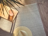 A beige cotton rug on a wooden floor, surrounded by natural elements.