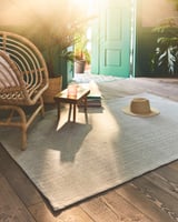 Bright room with wicker chair, small table, hat, and blue-green rug.