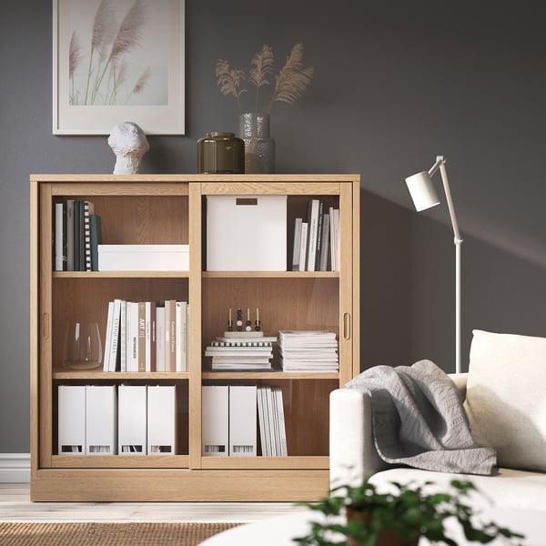 Cozy living room featuring TONSTAD oak bookcase, filled with books, and a white armchair, set against dark walls.