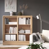 Cozy living room featuring TONSTAD oak bookcase, filled with books, and a white armchair, set against dark walls.
