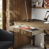 Wooden desk with open drawer, lamp, and tablet holder, showcasing organized workspace setup.