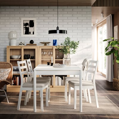 Modern dining setup with white TONSTAD table and chairs, brick wall, wooden cabinet, black pendant light, rug, and plants.